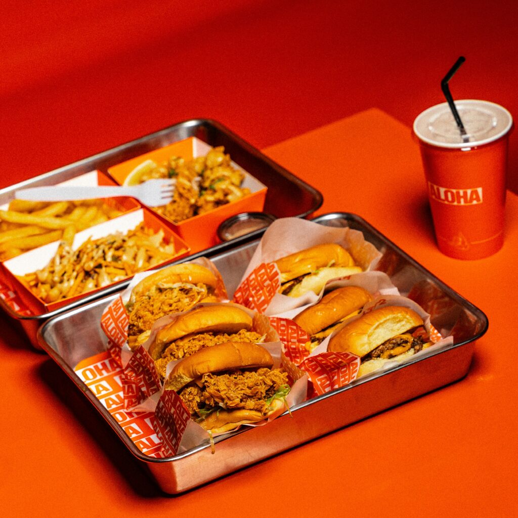 A tray of various sandwiches with fried chicken, served alongside fries and a container of salad, delivered by a Southern California restaurant platform.