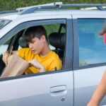 man in yellow shirt sitting inside a car looking into a paper bag